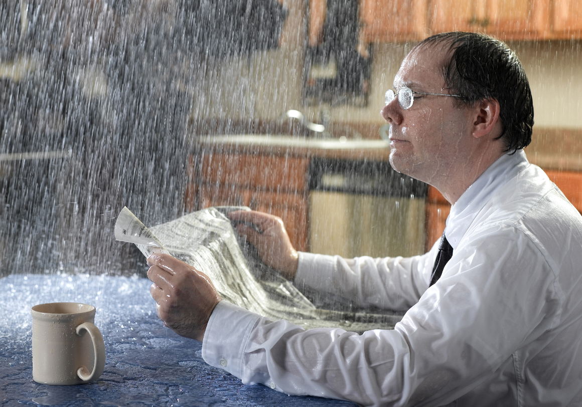 roof-leaking-raining-indoors Man in suit being rained on in their house due to roof leak
