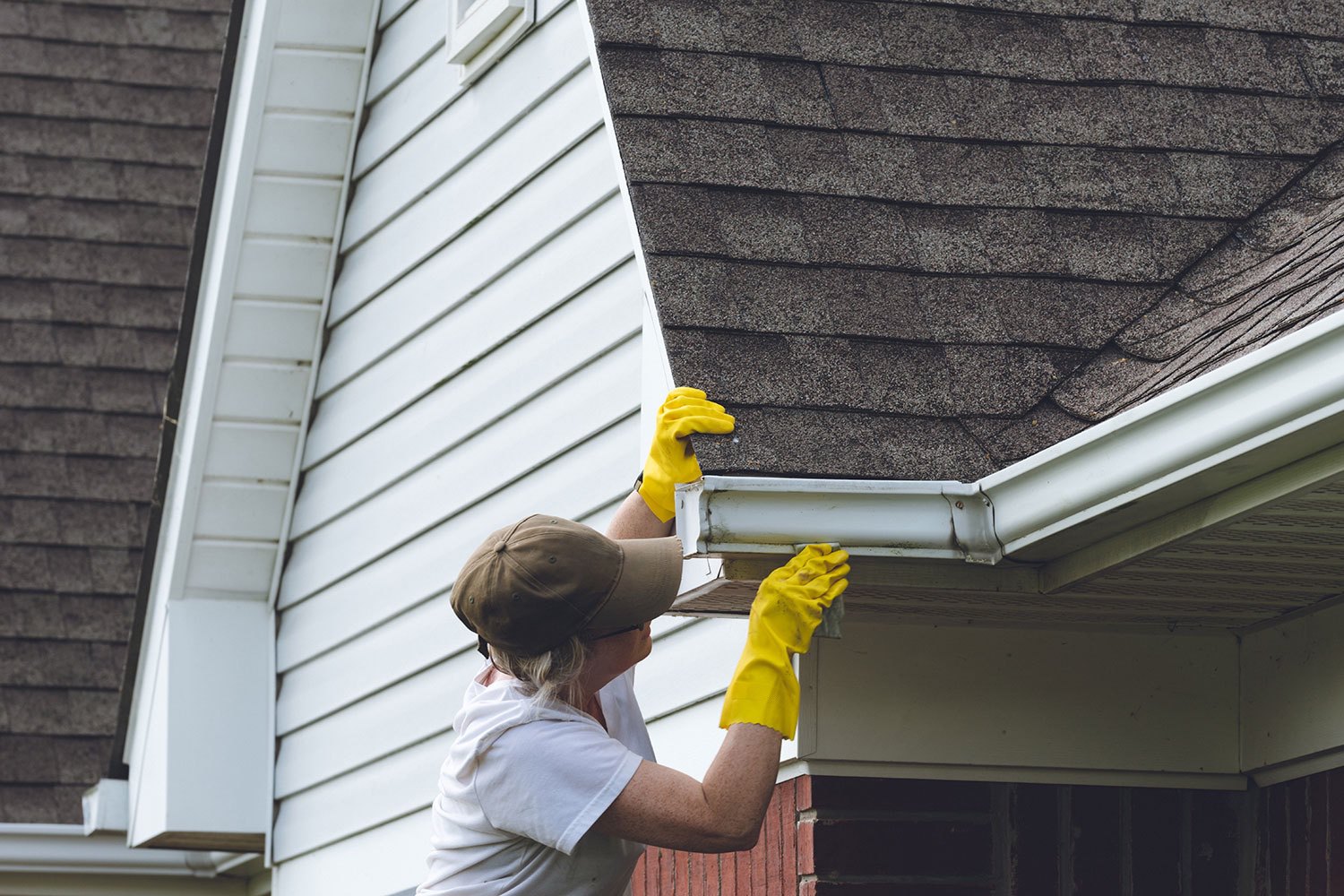 Person with gloves cleaning eavestroughs on Calgary home