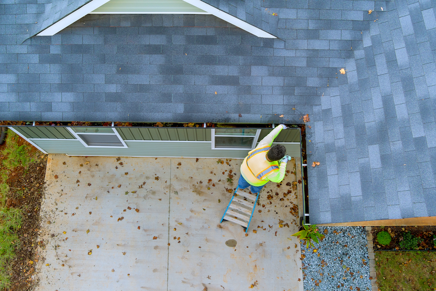 Man standing on a ladder and cleaning out the house gutters